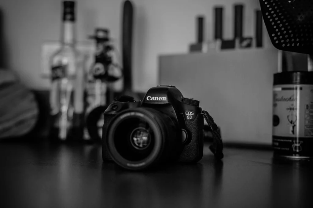 Чорно-біла фотографія повнокадрової дзеркальної камери Canon EOS 6D з встановленим світлосильним об'єктивом 50mm, яка лежить на столі поруч із кавовими аксесуарами